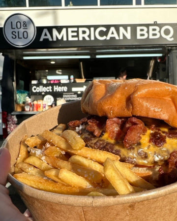A delicious looking burger and fries held up in front of a black food truck.