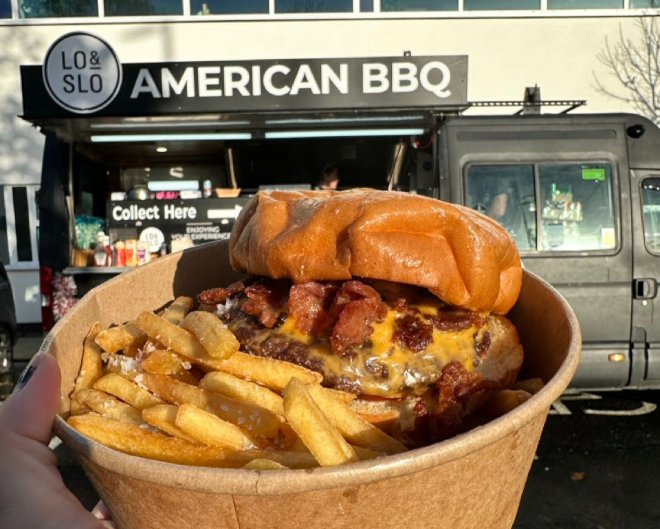 A delicious looking burger and fries held up in front of a black food truck.